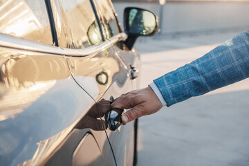 Portrait of man car owner opening door of his automobile outdoors in daytime.