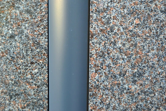 A new flat steel downpipe is embedded in a gray granite wall