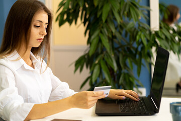 Young woman holding a credit card and using a laptop making an online payment in the office. Online shopping