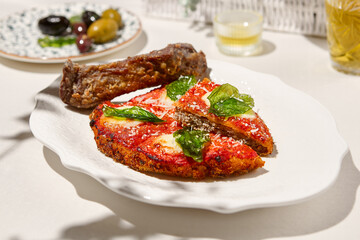 Traditional italian dish - milanese steak in breaded and parmesan on white ceramic plate. Milanese beef with tomato sauce and basil. Italian beef steak alla schnitzel with bone. Italian chop beef.