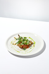 Baked eggplant with cheese on white table with harsh shadows. Aesthetic italian food - baked aubergine on white plate. Stuffed eggplant in minimal style. Stuffed aubergine in vegan menu.