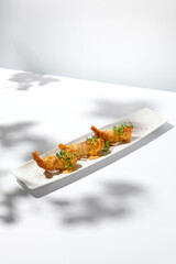 Traditional greek appetizer - kataifi wrapped shrimps on white plate. Crispy shrimp in kataifi crust in summer day. Shrimp appetizer fried in kataifi dough. Crispy prawns in modern style.