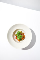 Crispy eggplant in chinese style on white plate. Crispy eggplant salad on summer menu. Asian appetizer - roasted aubergine with coriander leaves. Vegan food. Aesthetic veggie menu.