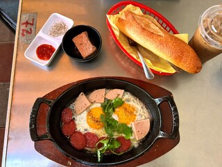 Vietnamese breakfast with eggs sunny side up with sausages, pate in an iron skillet and banh mi bread