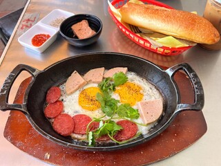 Vietnamese breakfast with eggs sunny side up with sausages, pate in an iron skillet and banh mi bread