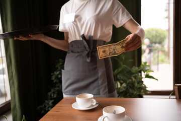 Woman hand taking tip US dollar banknotes from wooden table at cafe. payment, service charge, bill...