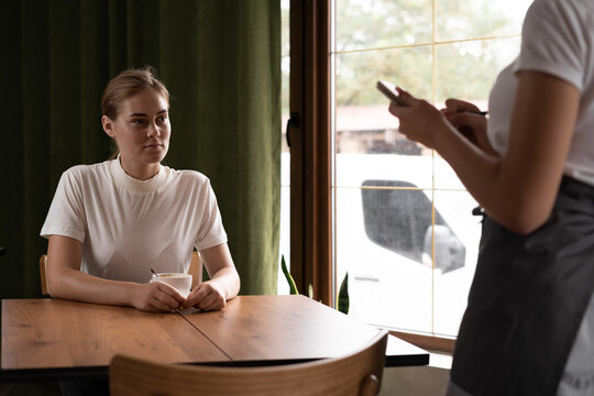 Friendly waiter writing down an order from a young woman in a coffee shop