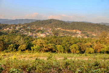 Lush Green Landscape with a Distant Town, Sunlight, and Dense Forest in a Scenic View