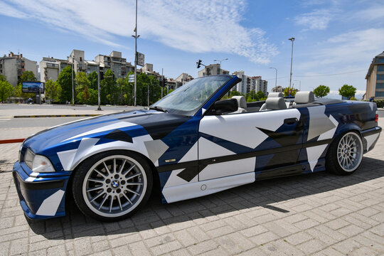 View of the sport car BMW 3 e36 cabriolet with sport rims and covered with decals parked in the street.