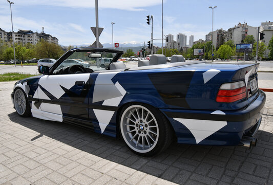View of the sport car BMW 3 e36 cabriolet with sport rims and covered with decals parked in the street.