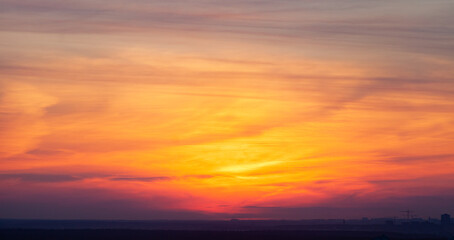 The blurry gradient background of the setting sun in the open air. The silhouettes of houses and cranes on the horizon.