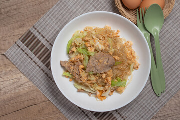 Stir fried vermicelli with pork, egg and collard greens in a white plate.