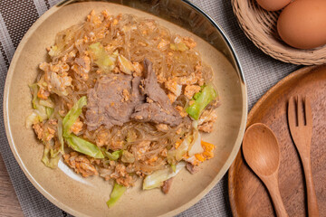 Stir fried vermicelli with pork, egg and collard greens in a white plate.