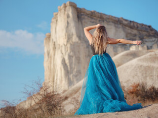 Fashionable woman on desert field near mountain wearing black top and blue tulle skirt - 525484870