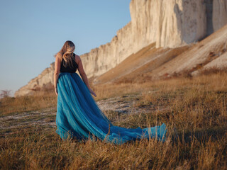Fashionable woman on desert field near mountain wearing black top and blue tulle skirt - 525484873