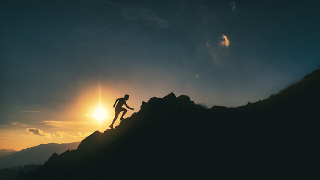Man climbs a rocky mountain ridge in a picturesque sunset