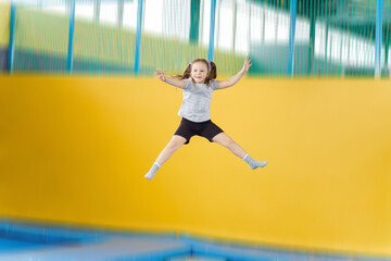 Happy little girl jumping on trampoline in fitness center