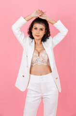 Portrait studio shot of Asian sexy curly hairstyle professional successful businesswoman in white fashionable casual suit with lace lingerie crop top bra standing look at camera on pink background