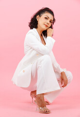 Portrait full body studio shot of Asian young sexy curly hairstyle businesswoman in white fashion casual suit high heels sitting smiling look at camera kneel down posing on floor on pink background