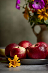 A bright bouquet of flowers in a ceramic vase and red ripe apples. Stylish and cozy autumn still life with fruit