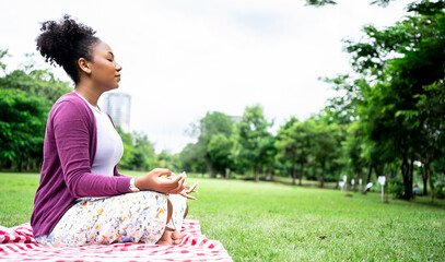 African woman practices yoga and meditates in the lotus position at park. Attractive woman sitting...
