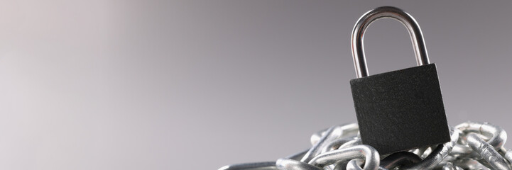 Solid metal locked padlock on top of tangled silver chain