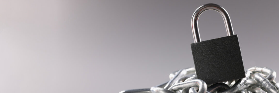 Solid metal locked padlock on top of tangled silver chain