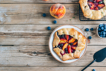 Galette, rustic sweet open pie with peach and blueberry on gray marble background.