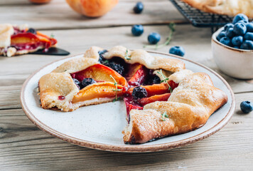 Galette, rustic sweet open pie with peach and blueberry on gray marble background.