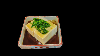 Isolated Tofu Topped with Seaweed and sauce on black background.