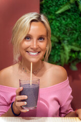 Woman smiling while drinking a smoothie in a coffee shop. Healthy lifestyle concept.