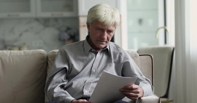 Focused Grey Haired Older Man Reading Bad News In Paper Document At Home, Turning From Serious To Shocked, Anxious, Upset, Getting Concerning Medical Test Result, Bankruptcy Notice, Rejection