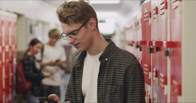 Sad Teenager Reading On Phone At School Cyber Bully Or Online At High School. Nerd Or Geek Feeling Bad With Anxiety, Mental Health And Angry With Social Media Post And Children Laughing In The Hall