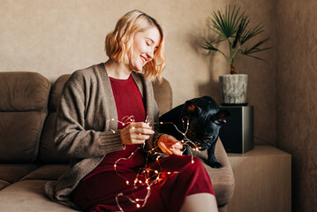 Young woman preparing for christmas and holding garland with lights. Xmas spirit in cozy modern home indoors. Portrait of people waiting holidays