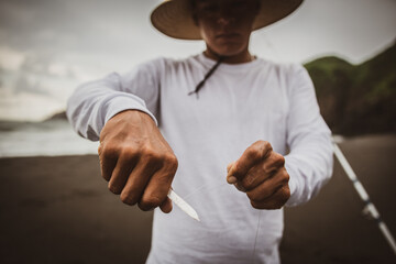 Unrecognizable fisher cutting fishing line on coast