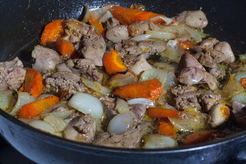 Cooking fried liver with vegetables in a black frying pan