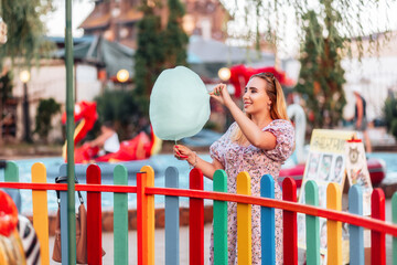 Summer festival. Dreamy pretty woman eating a cotton candy at amusement park. The concept of...