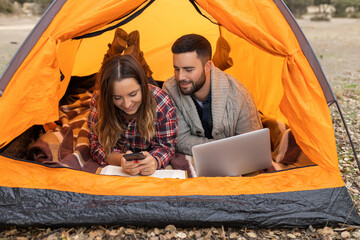 Camping couple inside tent using gadgets