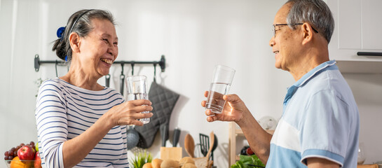 Asian senior elderly couple drink a glass of water in kitchen at home. 