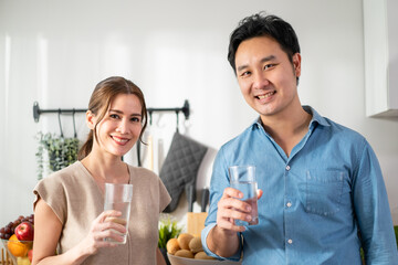 Asian attractive couple drinking a glass of water in kitchen at home. 