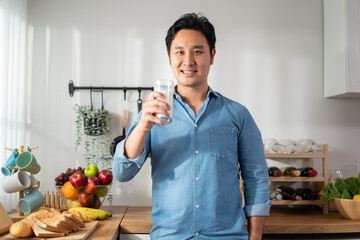 Portrait of Asian young man drinking glass of milk in kitchen at home.