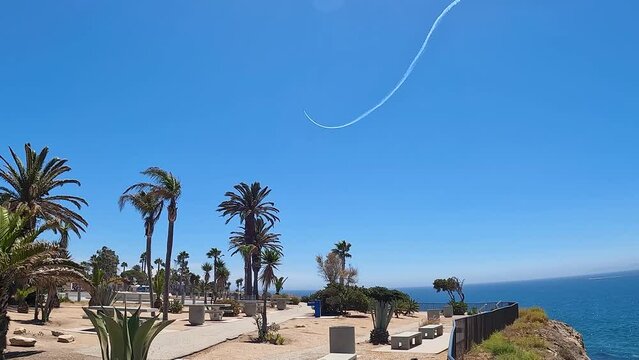 a gorgeous summer landscape at the beach with blue ocean water and lush green palm trees and plants with a skywriter in the clear blue sky writing at White Point Beach in San Pedro California USA