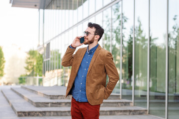 Focused young businessman in sunglasses with smart phone, involved in call negotiations meeting with partners colleagues or studying distantly