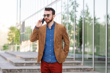 Fototapeta premium Focused young businessman in sunglasses with smart phone, involved in call negotiations meeting with partners colleagues or studying distantly