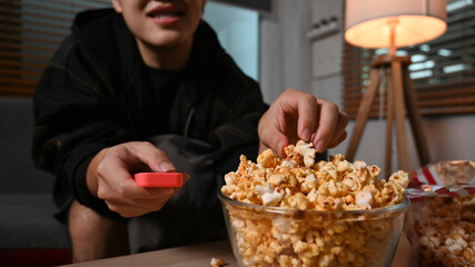 Cropped shot of man eating popcorn and watching television in cozy living room at night. Leisure activity, relaxation, hobby concept