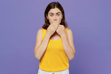 Young sad shocked surprised scared woman 20s she wearing yellow tank shirt cover mouth with hand look camera isolated on plain pastel light purple background studio portrait. People lifestyle concept.