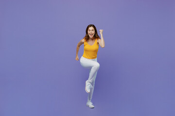 Fototapeta na wymiar Full body young smiling happy woman 20s she wear yellow tank shirt look camera clench fist run fast hurry up isolated on plain pastel light purple background studio portrait. People lifestyle concept.