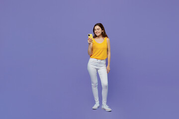Full body young fun woman 20s she wear yellow tank shirt hold in hand use mobile cell phone chatting in social network isolated on plain pastel light purple background studio People lifestyle concept