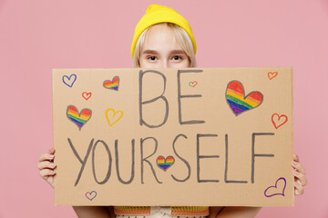 Young fun blond lesbian woman she wear colorful knitted top hat hold cover mouth with cardboard...