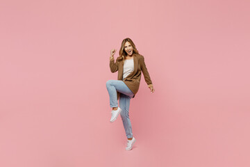 Full body young successful employee business woman 30s she wear casual brown classic jacket do winner gesture clench fist raise up leg isolated on plain pastel light pink background studio portrait.